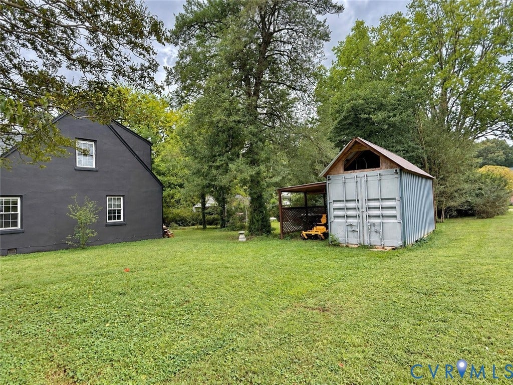 518 Central Terrace, Hopewell, VA 23860 Expansive grassy area with mature trees, featuring a dark-toned exterior structure with white-framed windows, and a separate storage structure with an attached covered area
