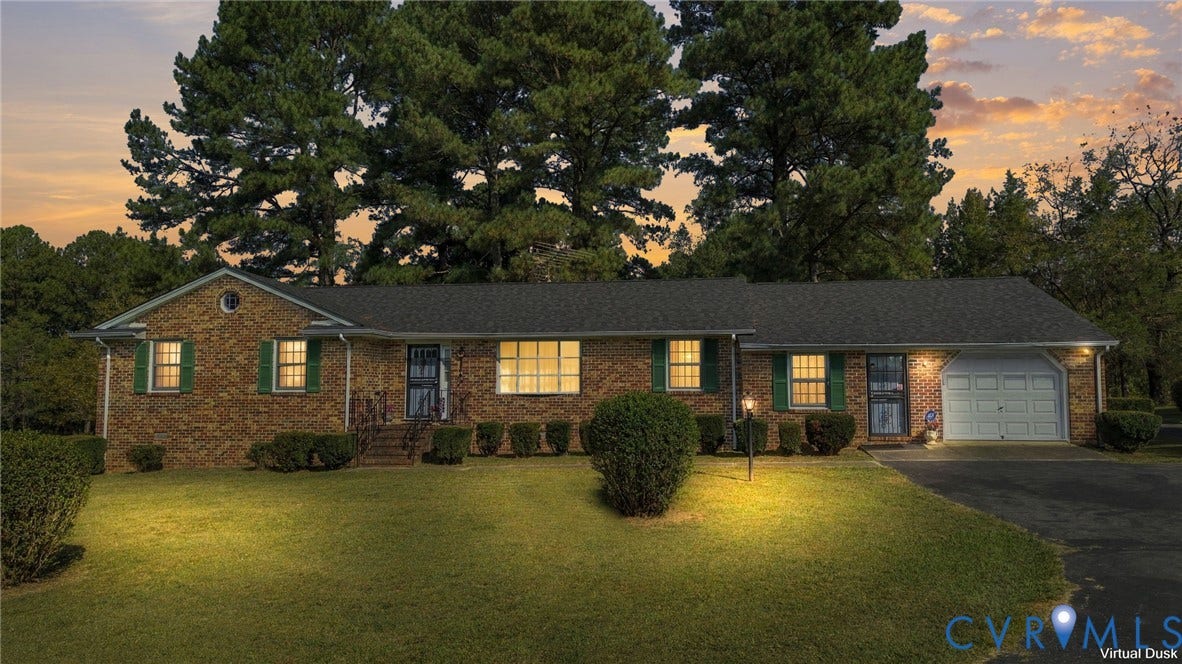 Brick exterior with a dark shingle roof, attached garage, green shutters, and a paved driveway