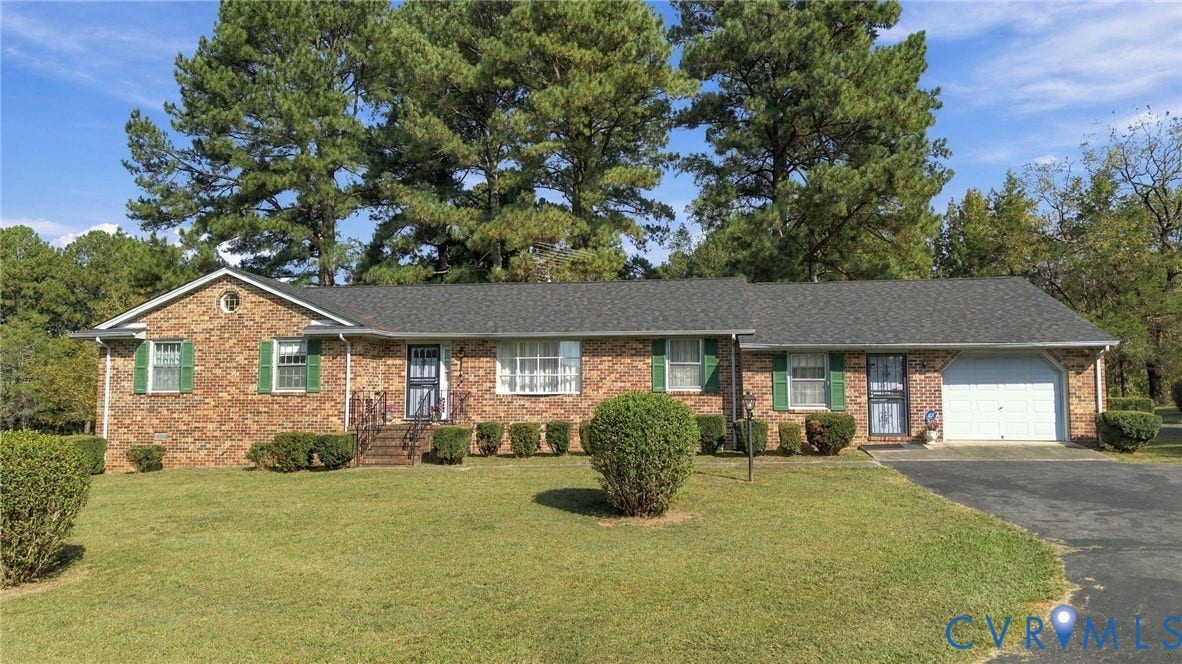 Brick exterior with a dark shingle roof, attached garage, paved driveway, and mature landscaping