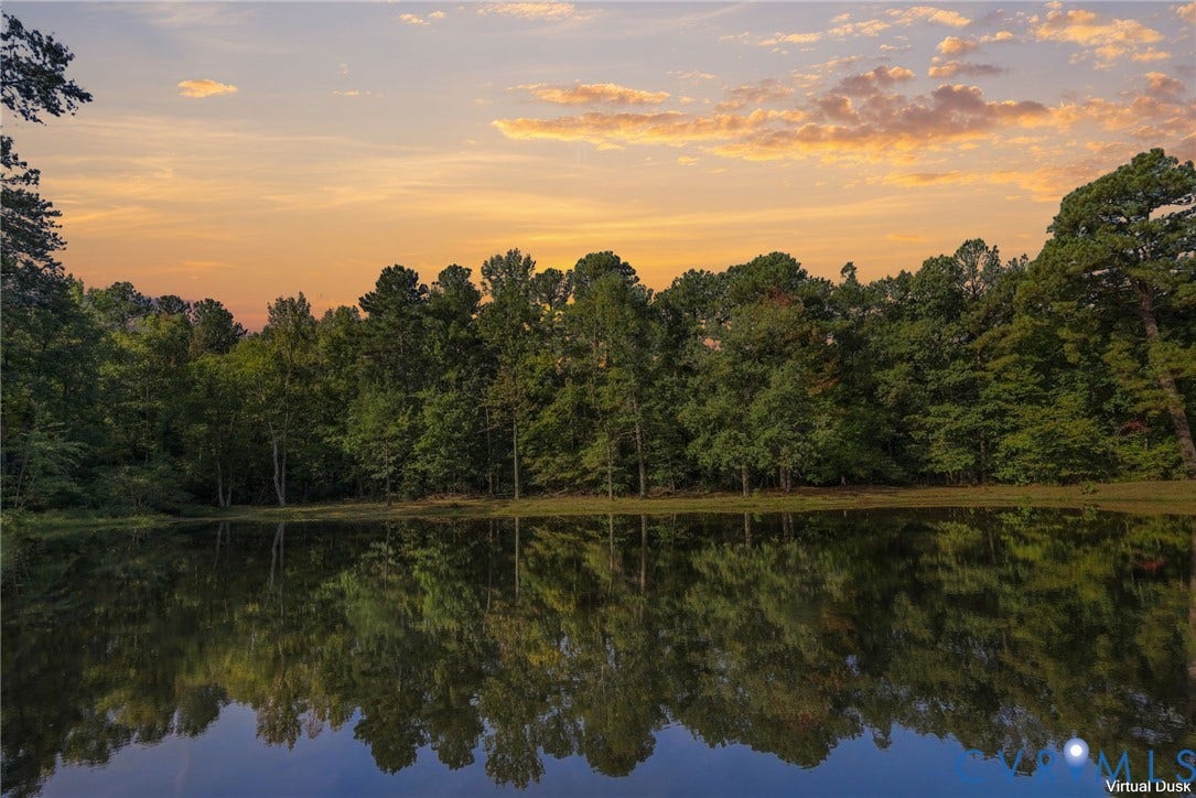 Expansive body of water reflecting surrounding mature trees under a colorful sky