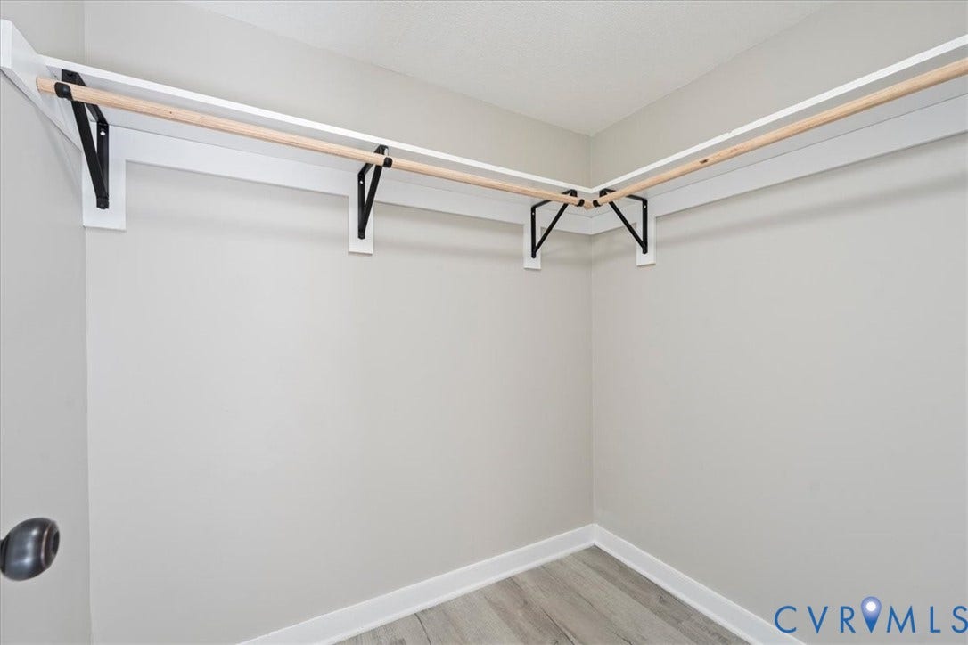 115 Mount Airy Lane, Cumberland, VA 23040 Spacious walk-in closet featuring wood-finish flooring, pristine white walls, and a comprehensive rod and shelf system with multiple hanging stations and storage brackets for optimal organization