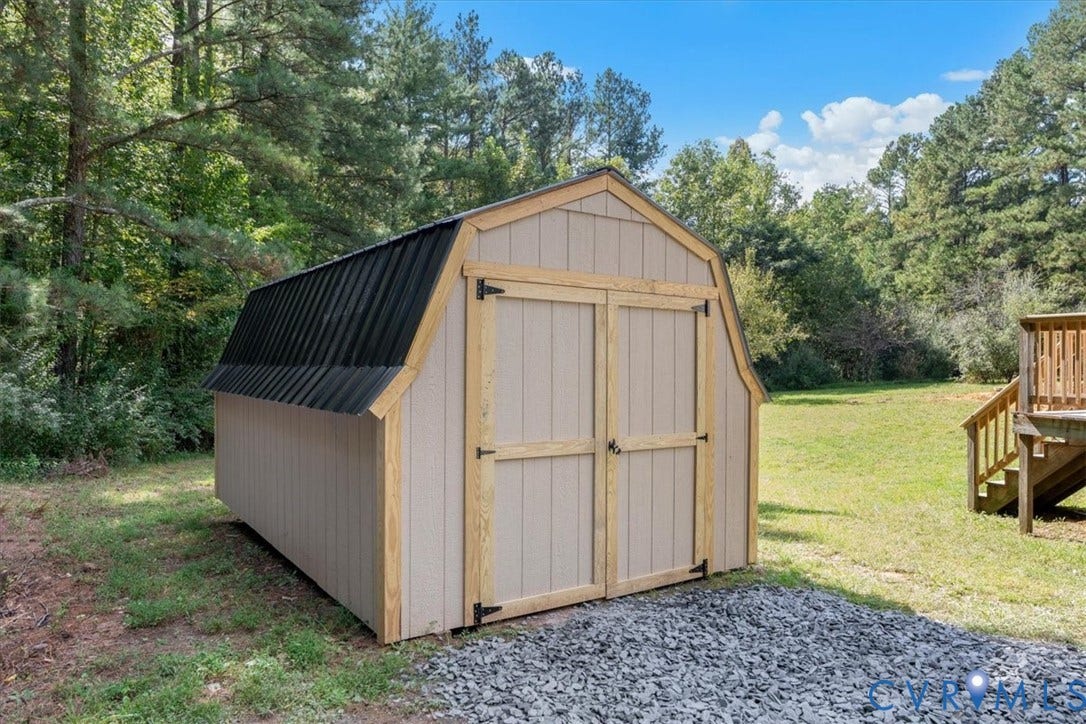 115 Mount Airy Lane, Cumberland, VA 23040 Charming storage shed featuring a classic barn-style roof with black metal roofing, cream-colored exterior walls, and double hinged doors with black hardware
