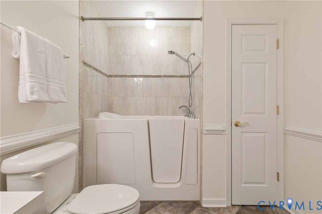 Walk-in bathtub featuring a handheld showerhead and tiled surround