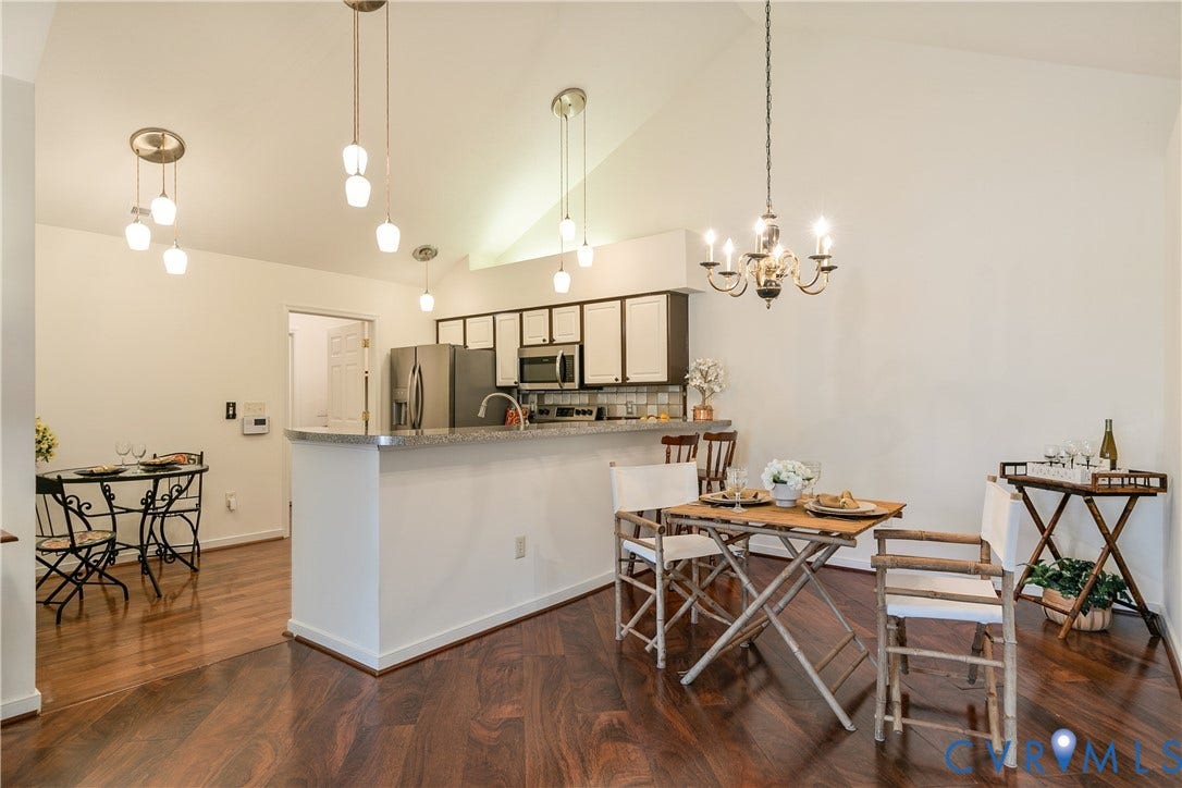 Vaulted ceiling, wood-finish flooring, two-tone kitchen cabinetry, stainless steel appliances, and a breakfast bar