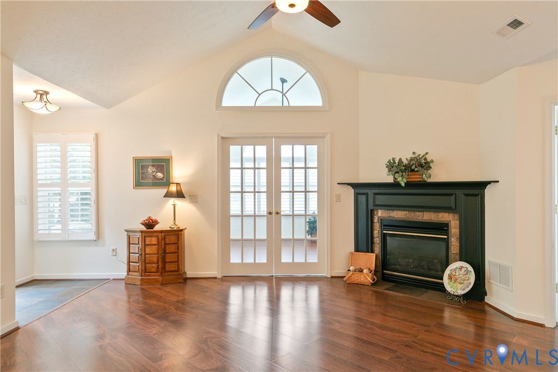 Vaulted ceilings with a ceiling fan, wood-finish flooring, a fireplace with a dark-finish mantel, and French doors with an arched transom window