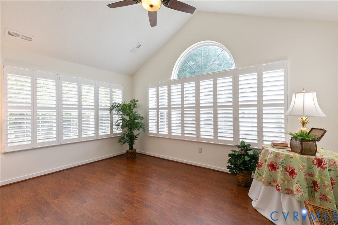 Vaulted ceiling with a ceiling fan, abundant natural light, wood-finish flooring, and multiple windows with plantation shutters