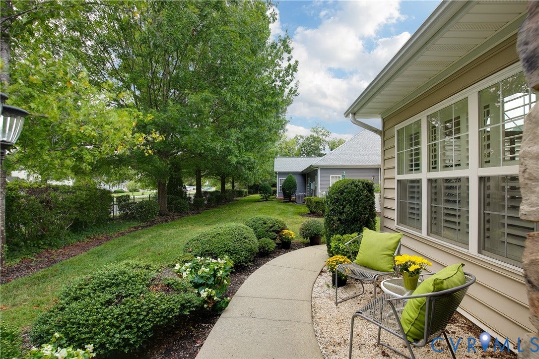Siding exterior, multi-pane windows with interior shutters, concrete walkway, gravel patio area, and mature landscaping