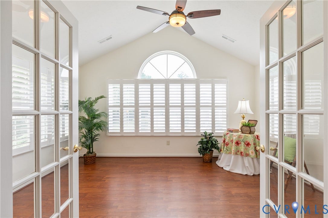 French doors opening to a room featuring a vaulted ceiling with fan, wood-finish flooring, plantation shutters, and an arched window