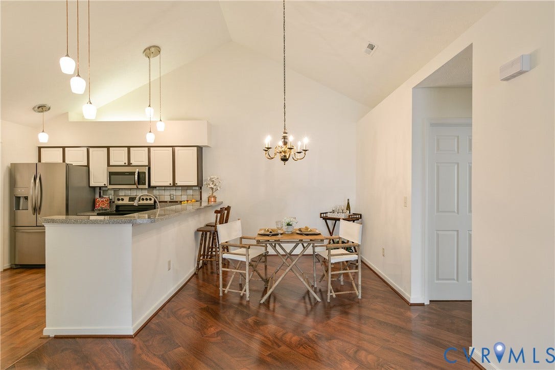 Vaulted ceilings complement wood-finish flooring throughout this open space, featuring a kitchen with stainless steel appliances, white cabinetry, and a light-toned countertop