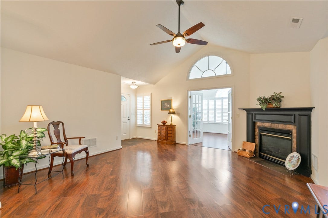 Vaulted ceiling with a ceiling fan, wood-finish flooring, fireplace with a dark mantel, French doors, and an arched transom window
