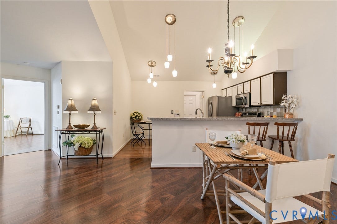 Wood-finish flooring, vaulted ceilings, and a kitchen featuring stainless steel appliances, white cabinetry, and a breakfast bar with a stone-finish countertop