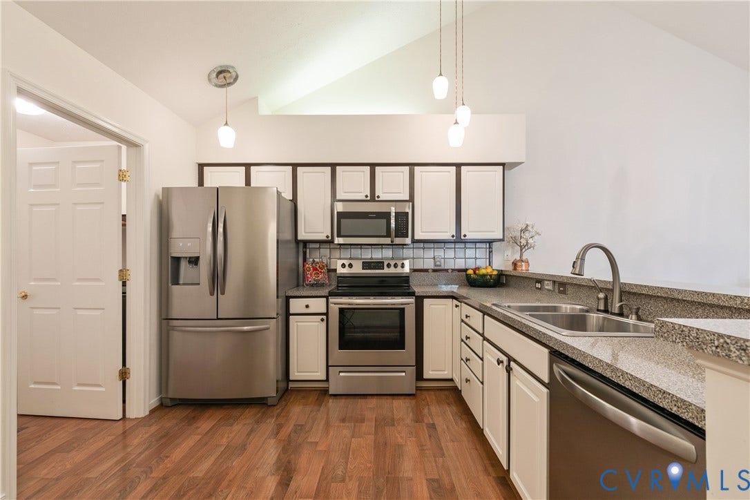 Kitchen featuring vaulted ceilings, wood-finish flooring, stainless steel appliances, and light-toned cabinetry with dark hardware
