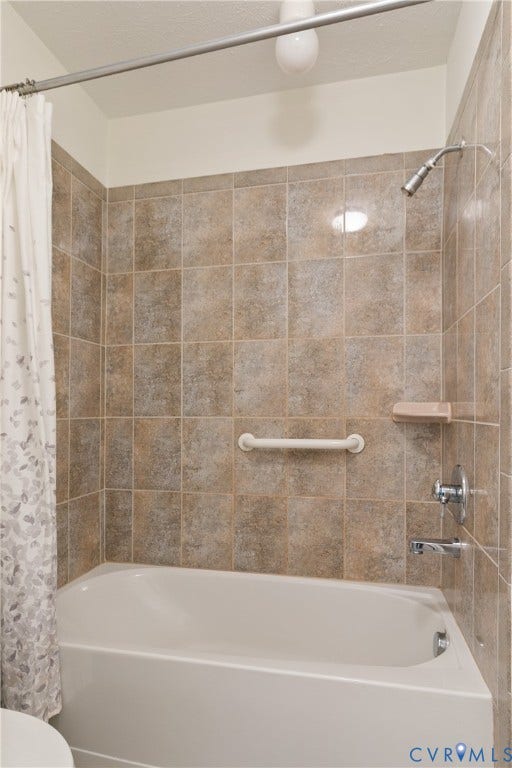 Tiled shower surround with a built-in tub, chrome fixtures, and an integrated grab bar