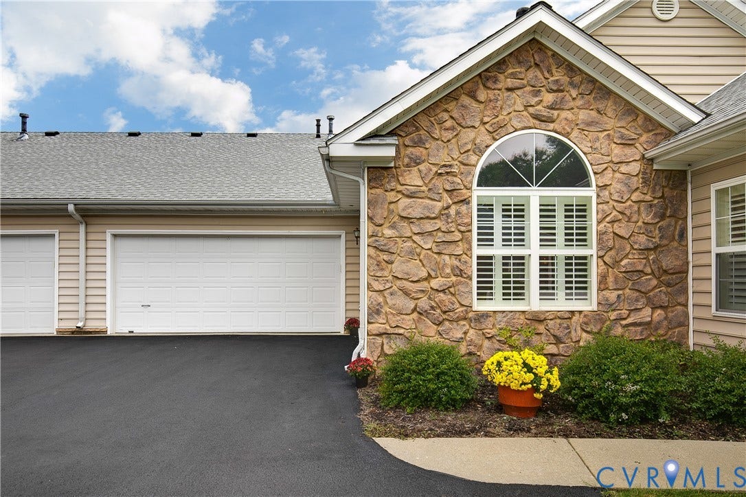 Stone veneer facade, arched window with decorative muntins, white window shutters, two-car garage, and asphalt driveway