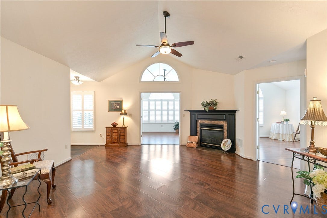 Vaulted ceilings with a ceiling fan, wood-finish flooring, a fireplace with a black mantel, and an arched transom window