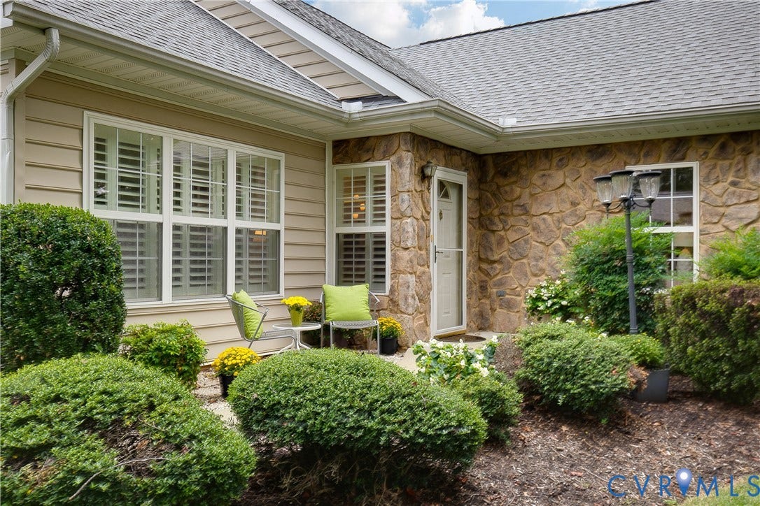 Stone veneer facade, horizontal siding, white-framed windows with louvered shutters, asphalt shingle roof, and established landscaping