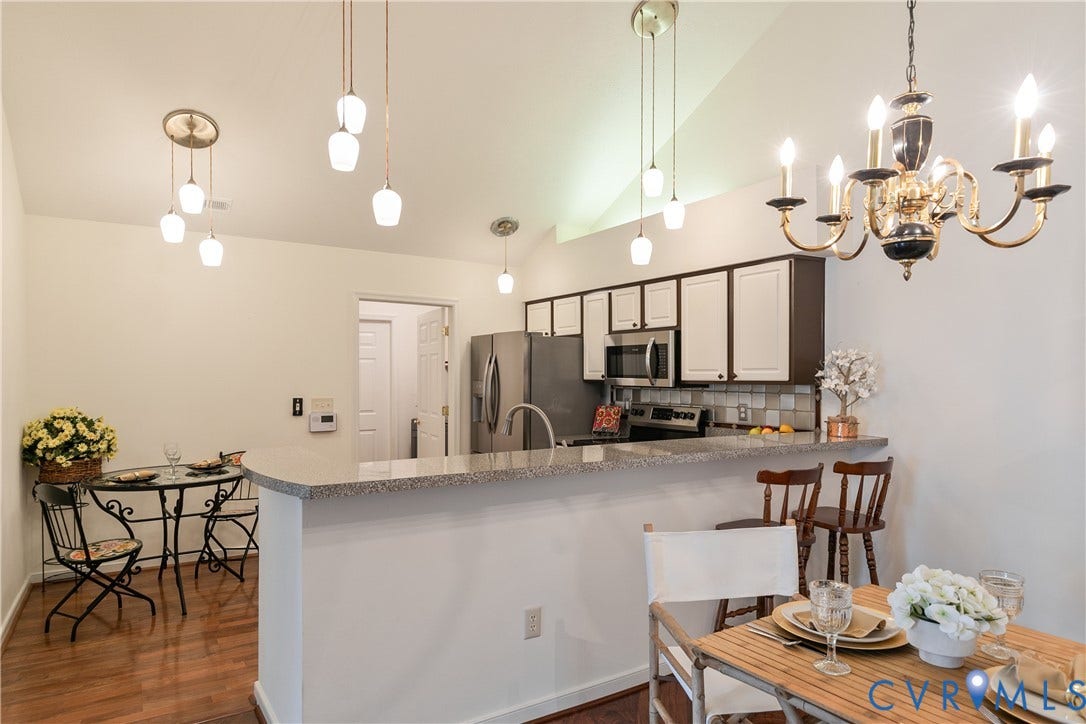 Vaulted ceiling with multiple pendant lights and a chandelier, kitchen featuring stainless steel appliances, two-tone cabinetry, and a tile backsplash, and a breakfast bar with stone-look countertop