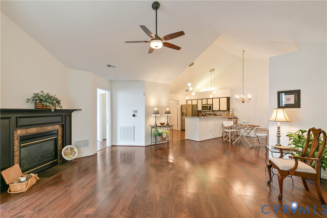 Vaulted ceilings, wood-finish flooring, built-in fireplace with mantel, ceiling fan, and open-concept kitchen with pendant lighting