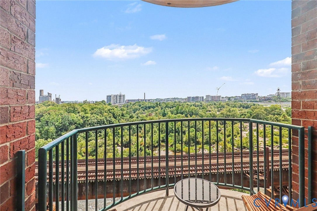 1101 Haxall Point, #U512 U510, Richmond, VA 23219 Outdoor balcony featuring a metal railing, brick exterior, and a distant tree-lined landscape with urban structures