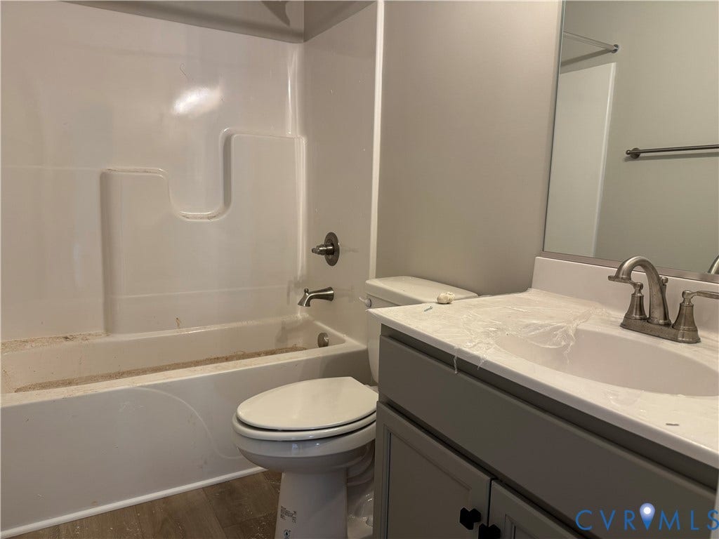 7735 Jefferson Highway, Cedar Hill Park, Mineral, VA 23117 Bathroom featuring a single vanity with a white countertop and undermount sink, brushed nickel faucet, gray cabinetry, built-in bathtub with shower, and wood-finish flooring