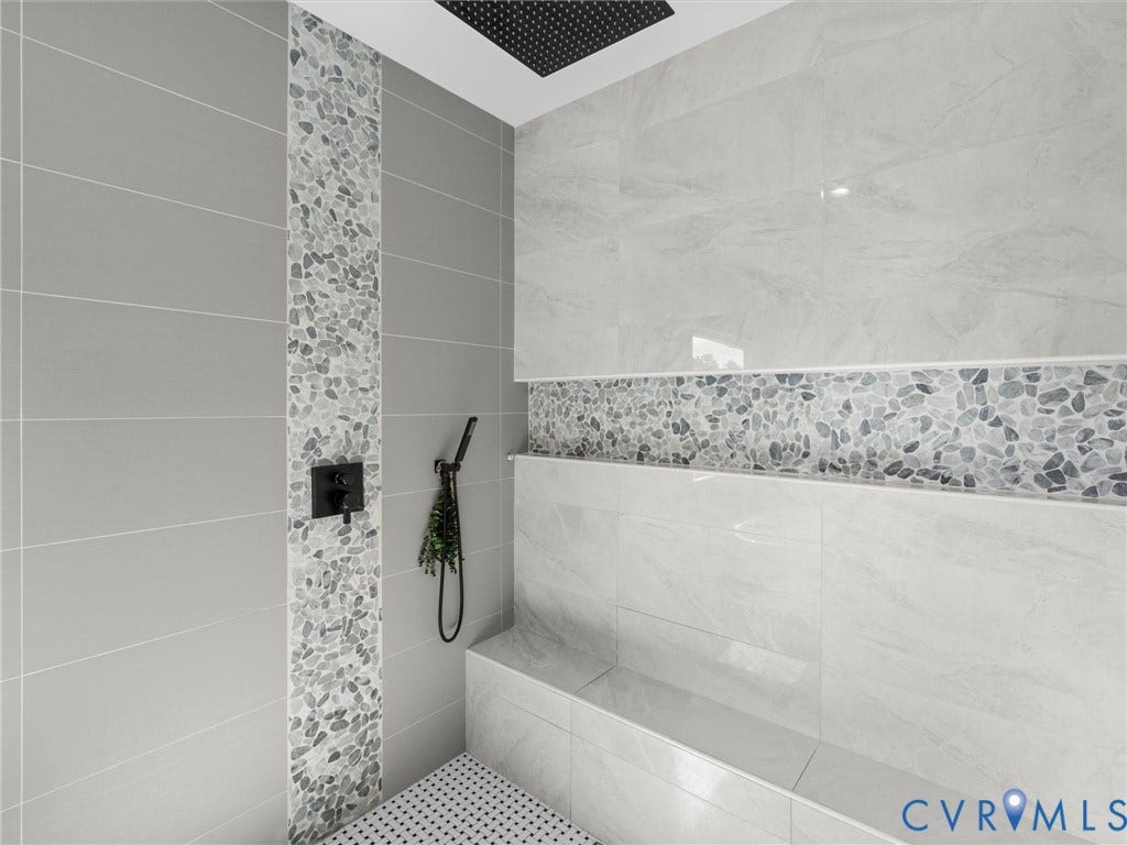 Spacious shower with large format grey tiling, pebble mosaic accents, and an integrated bench