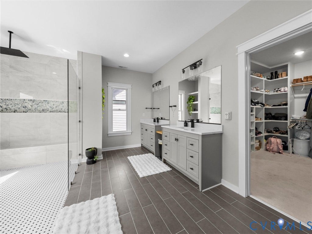 Dual vanity with integrated sinks, frameless glass shower enclosure, black finish showerhead, walk-in closet with built-in shelving, and wood-finish flooring