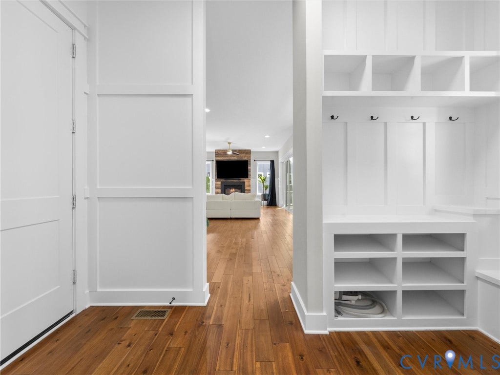 Built-in storage solutions, wood-finish flooring, white paneling, integrated coat hooks, and recessed lighting