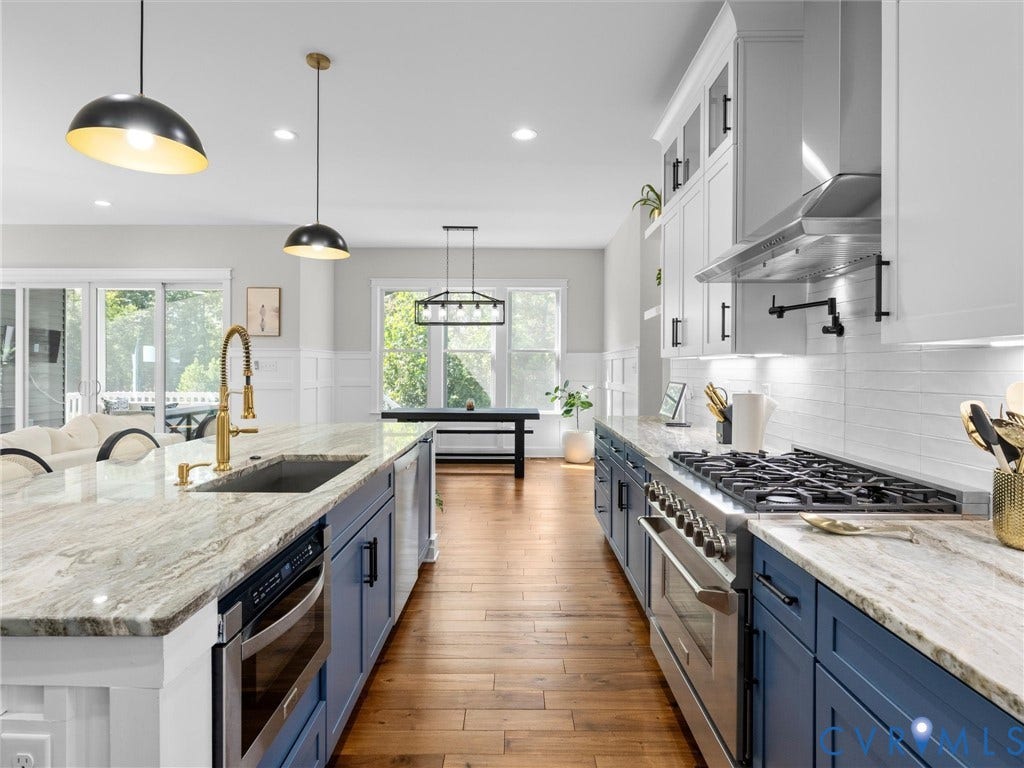 Gourmet kitchen featuring a large island, wood-finish flooring, stainless steel appliances, white subway tile backsplash, and two-tone cabinetry