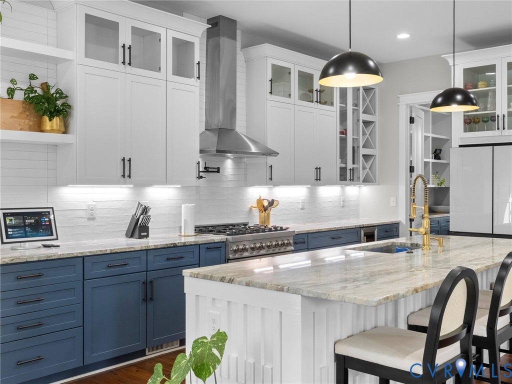 Two-tone cabinetry with white upper and blue lower cabinets, light-toned countertop, stainless steel range hood, built-in wine rack, and a gold-finish faucet