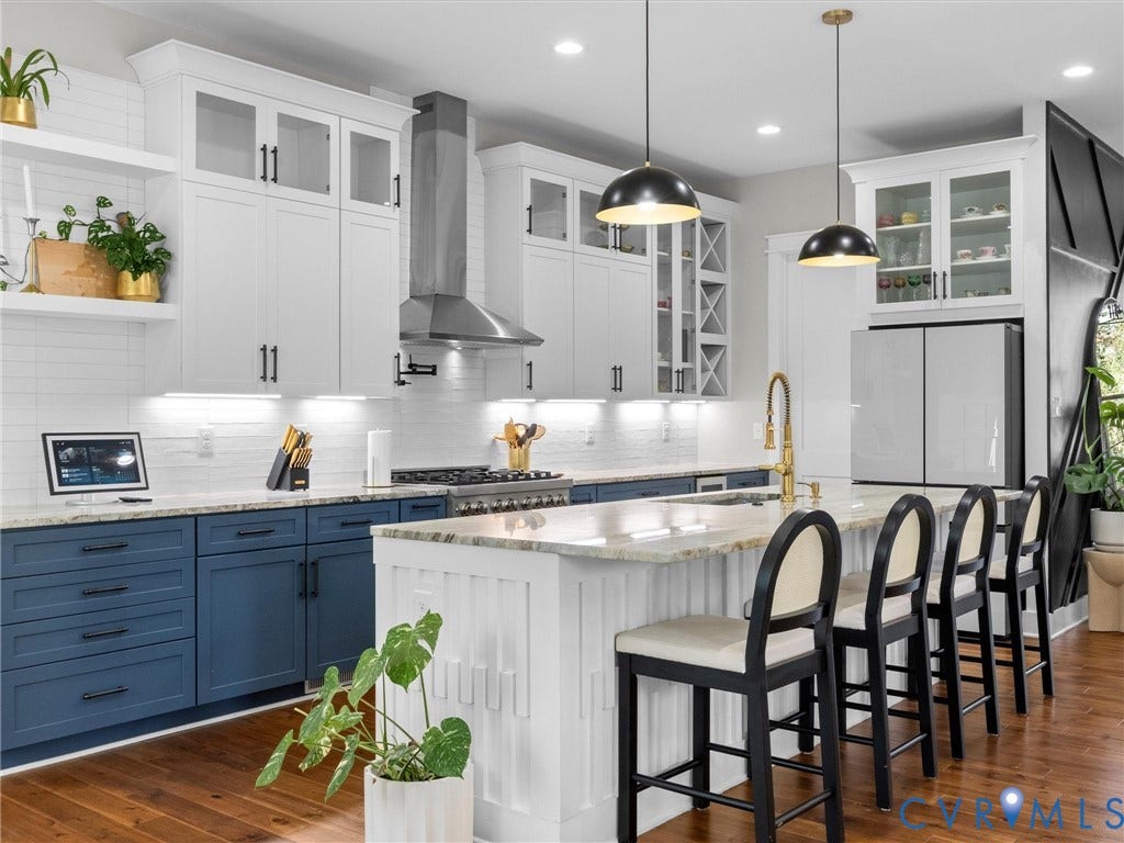 Gourmet kitchen featuring white and blue cabinetry, granite countertops, wood-finish flooring, a stainless steel range hood, and pendant lighting