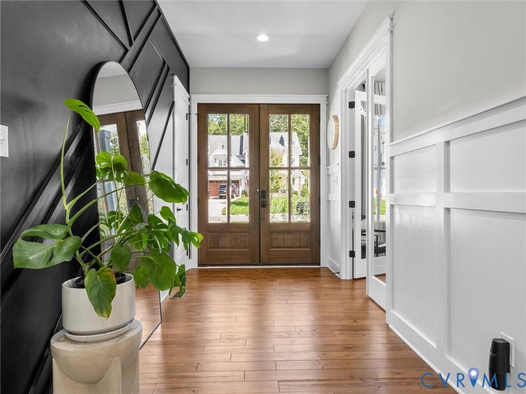 Hardwood flooring extending throughout, dark wood-finish double entry doors with integrated glass, white board and batten paneling, dark accent wall with geometric molding, and recessed lighting