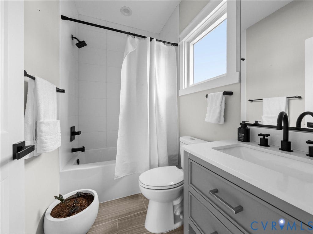 Bathroom with a white bathtub and shower featuring matte black fixtures, a single window, and a vanity with a white countertop and gray cabinetry