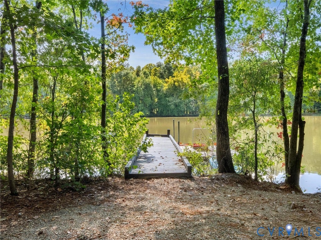 Waterfront access featuring a wooden dock, mature trees, and natural landscaping