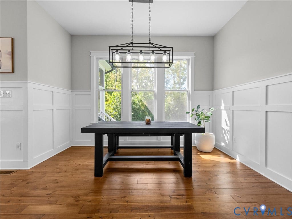Wood-finish flooring, wainscoting, and large windows with white trim
