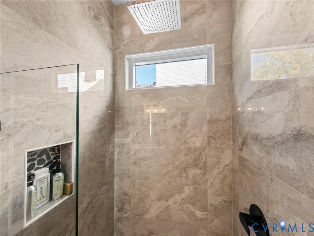 Shower featuring large format wall tiles, a built-in niche with pebble tile accent, a fixed pane window, and a square rainfall showerhead