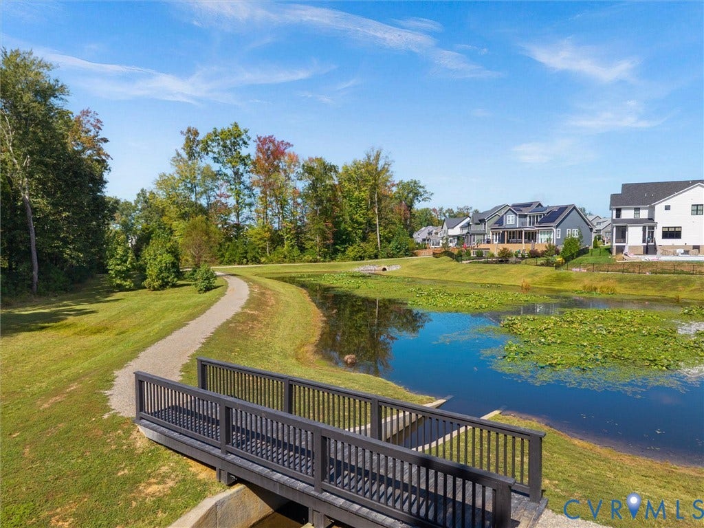 Pond with established lily pads, pedestrian bridge, and walking path surrounded by mature trees and manicured lawns