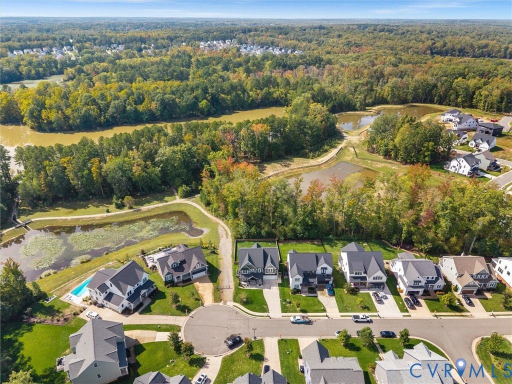 Aerial perspective of a residential neighborhood with private swimming pools, surrounded by mature trees and natural water features