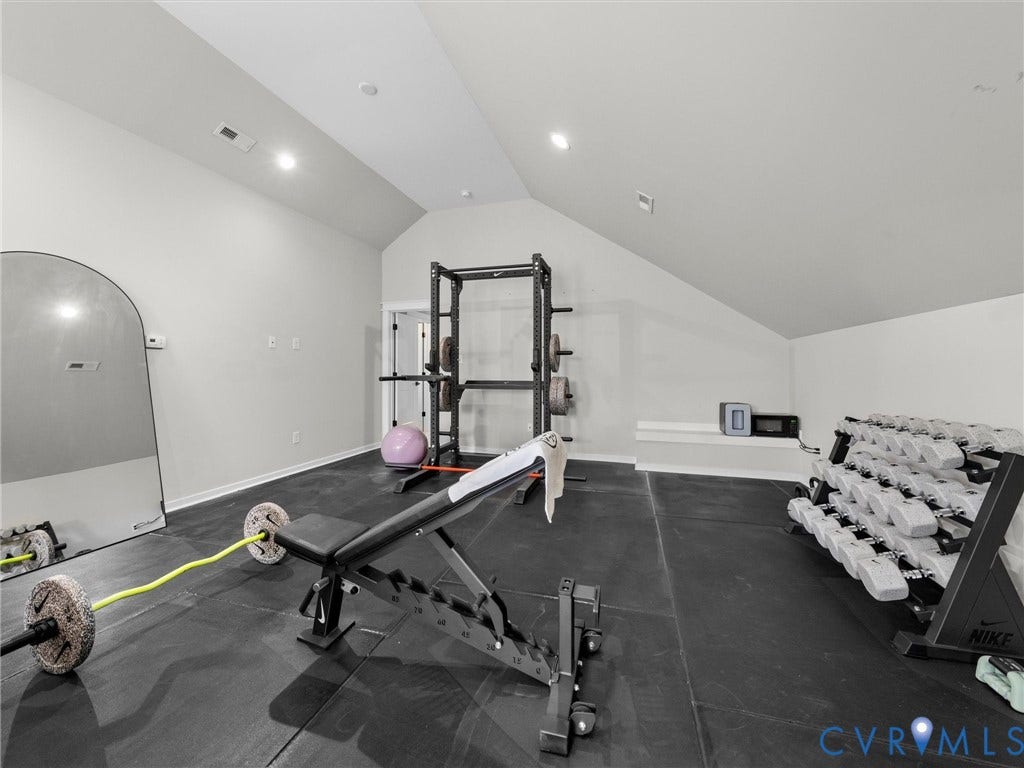 Dedicated fitness studio featuring polished dark flooring, recessed ceiling lighting, mirrored wall paneling, and integrated strength training equipment including a power rack, weight bench, and dumbbell storage system