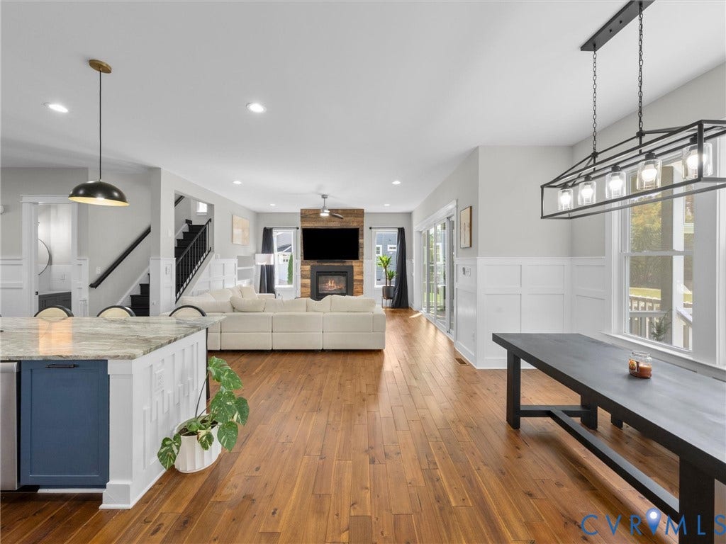 Open-concept living space featuring wood-finish flooring, a contemporary fireplace with a wood-paneled surround, and large windows