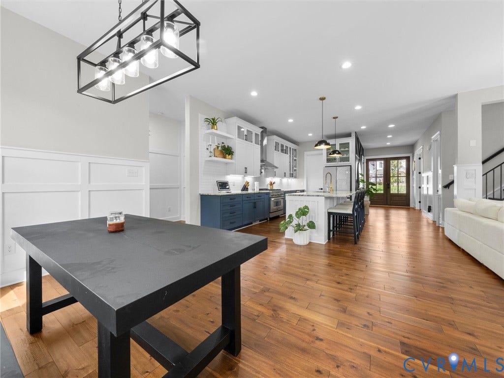 Wood-finish flooring throughout, modern kitchen island with seating, white shaker cabinetry, contrasting blue lower cabinetry, and double-pane entry doors