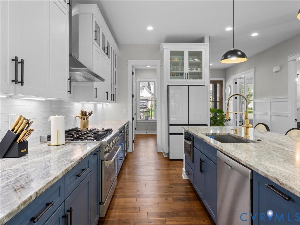Gourmet kitchen featuring a gas range, stainless steel appliances, two-tone cabinetry, and a large central island with an undermount sink