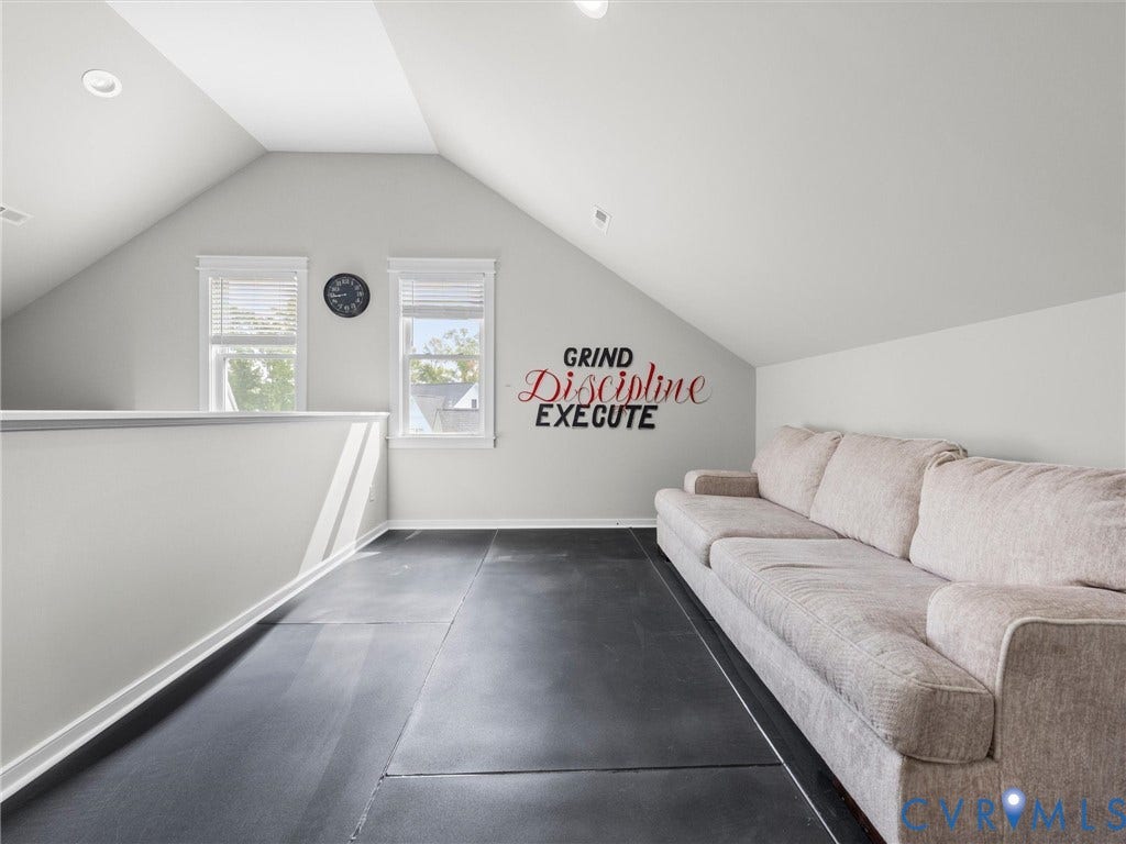 Sloped ceiling design, recessed lighting, dual windows with blinds, half-wall partition, and dark flooring