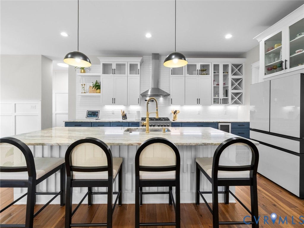 Kitchen featuring a large island with a stone countertop, two-tone cabinetry, stainless steel range hood, built-in wine storage, and wood-finish flooring