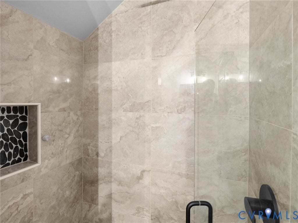 Shower enclosure with large format stone-look tiles, a built-in niche featuring dark pebble-look mosaic tiles, and a matte black shower fixture