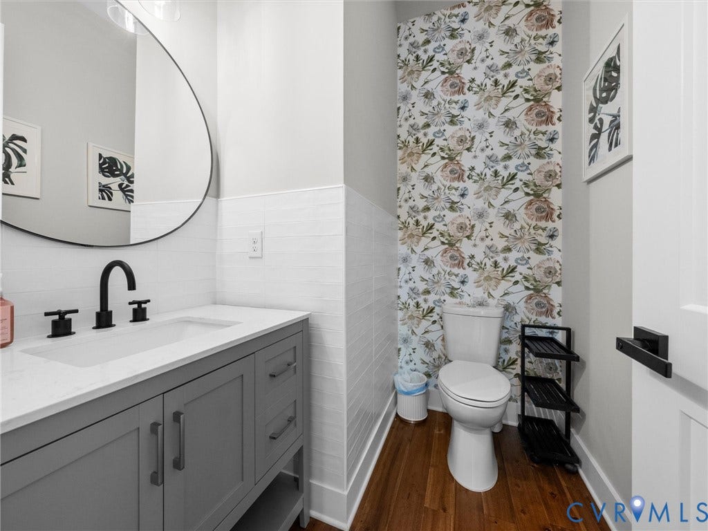 Vanity with white countertop, dark wood-finish flooring, white horizontal tile wainscoting, and floral accent wall