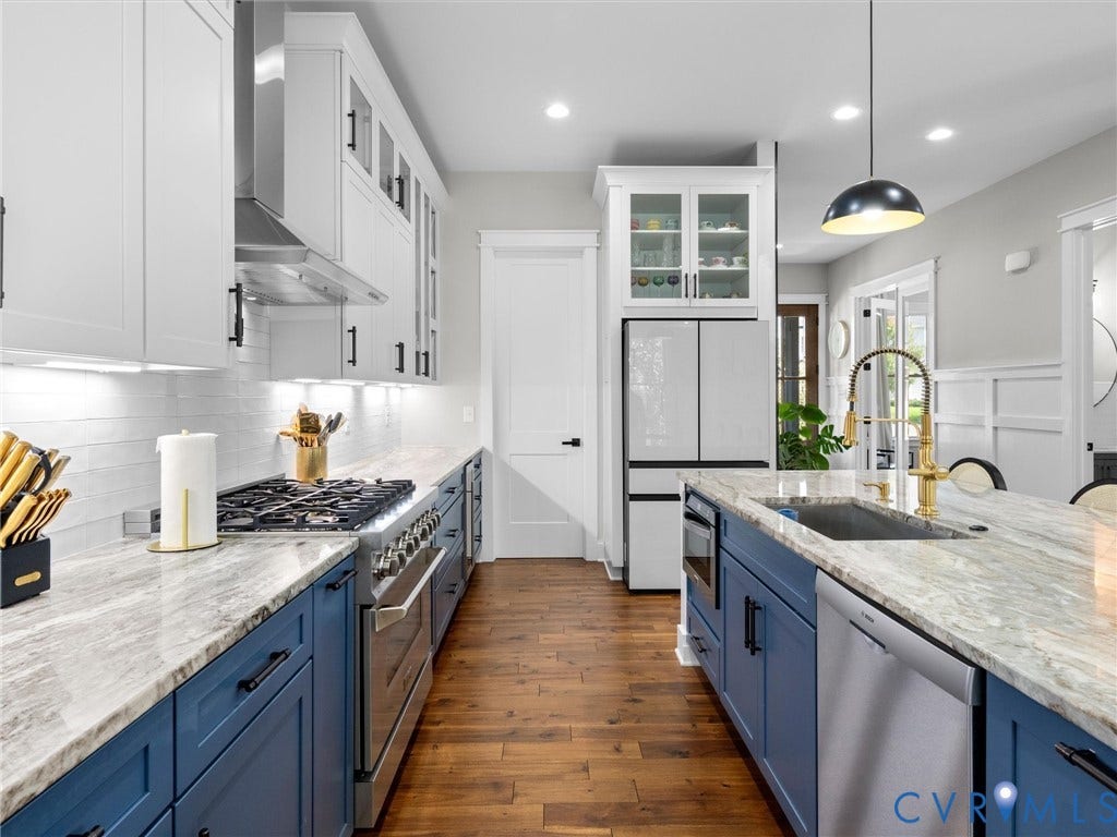 Gourmet kitchen featuring a gas range, custom two-tone cabinetry, stone countertops, stainless steel appliances, and wood-finish flooring