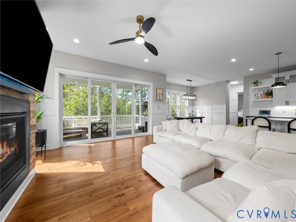 Hardwood flooring, fireplace with stone surround, screened porch with white railing, built-in recessed lighting, and a contemporary ceiling fan