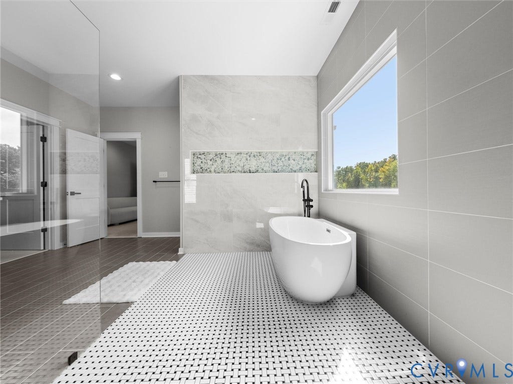 Freestanding bathtub with a wall-mounted matte black faucet, full-height wall tiling, and a recessed decorative tile accent