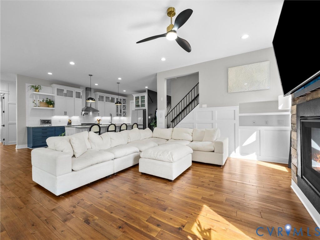 Open-concept living area featuring hardwood flooring, a ceiling fan with brass accents, recessed lighting throughout, and a gas fireplace