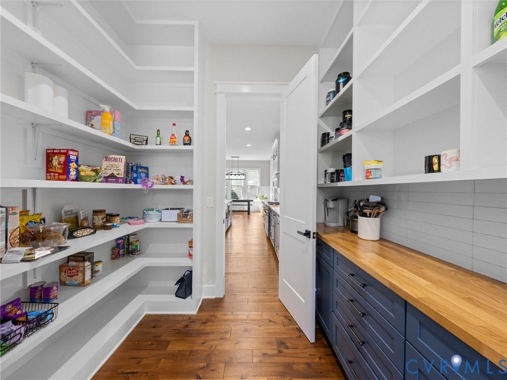 Built-in pantry shelving, wood-finish flooring, wood-finish countertop, blue cabinetry with dark hardware, and subway tile backsplash